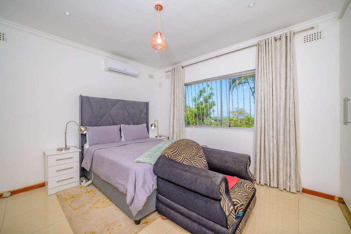 A well-maintained bedroom featuring tiled flooring, an air conditioning unit, recessed lighting, and built-in cupboards with security bars on the window.