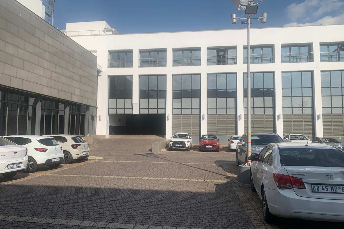 A modern multi-story office building exterior featuring a paved parking area and large glass facade windows.