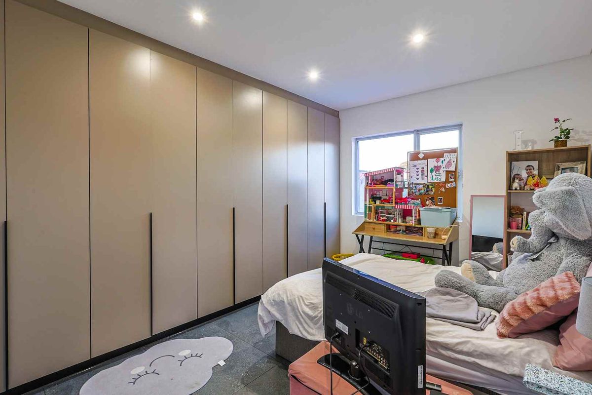 A well-maintained bedroom featuring extensive floor-to-ceiling built-in cabinetry with modern matte finish doors and large format floor tiles.