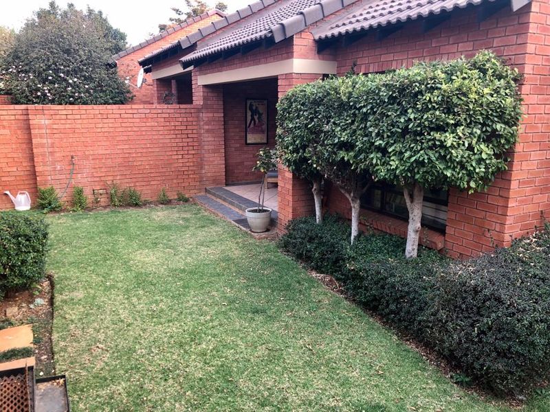 A private rear garden featuring a brick boundary wall, a covered patio area, and established landscaping adjacent to the townhouse structure.