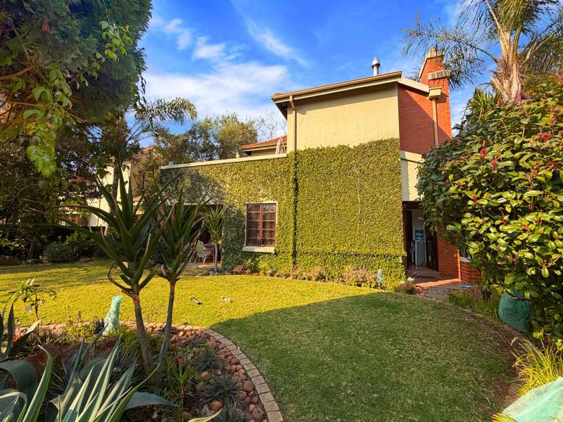 A view of the rear townhouse elevation featuring a covered patio, established garden, and brick chimney detail.