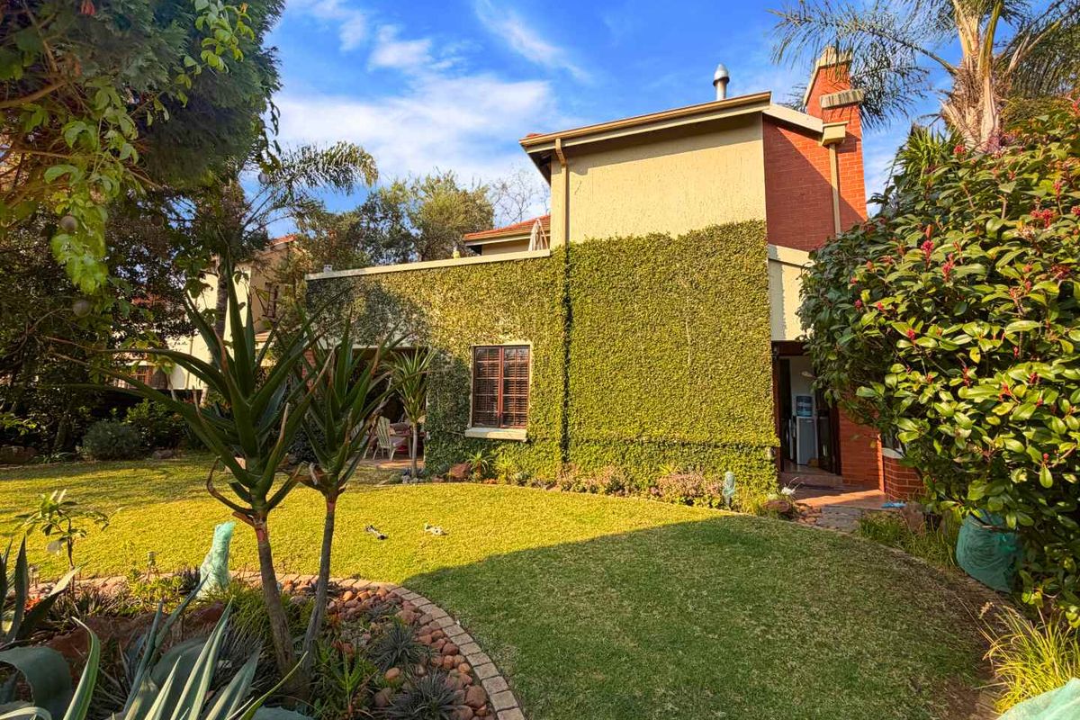 A view of the rear townhouse elevation featuring a covered patio, established garden, and brick chimney detail.
