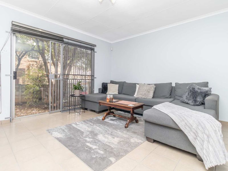 A bright living room featuring tiled flooring and a large sliding glass door with an integrated security gate, providing access to the outdoor area.
