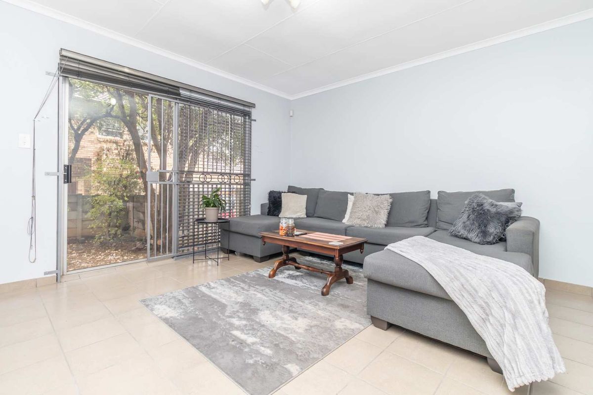 A bright living room featuring tiled flooring and a large sliding glass door with an integrated security gate, providing access to the outdoor area.