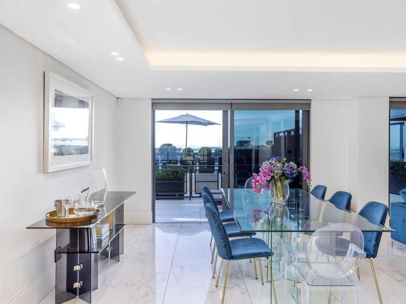 A bright, modern open-plan dining area featuring polished marble-look flooring, recessed ceiling lighting, and large sliding glass doors leading to an outdoor balcony.