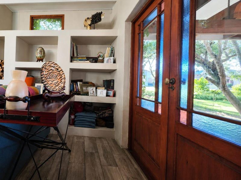 Entrance area featuring built-in shelving units, timber-framed glass double doors, and modern tiled flooring with a view to the garden.