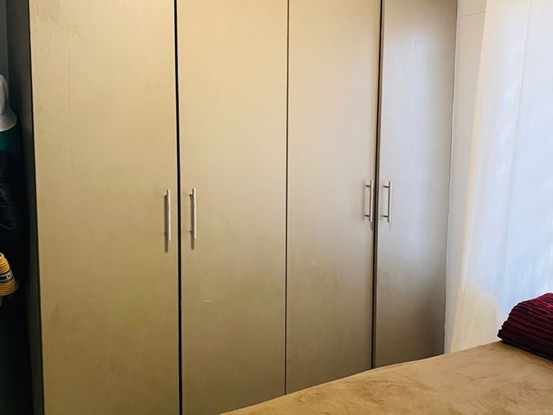 A bedroom featuring a large, full-height built-in wardrobe with modern handles and neutral finishes.