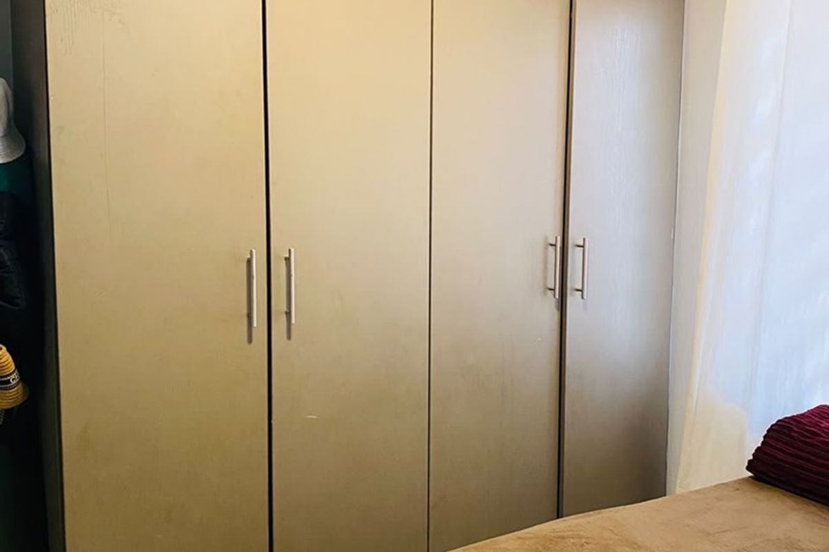 A bedroom featuring a large, full-height built-in wardrobe with modern handles and neutral finishes.