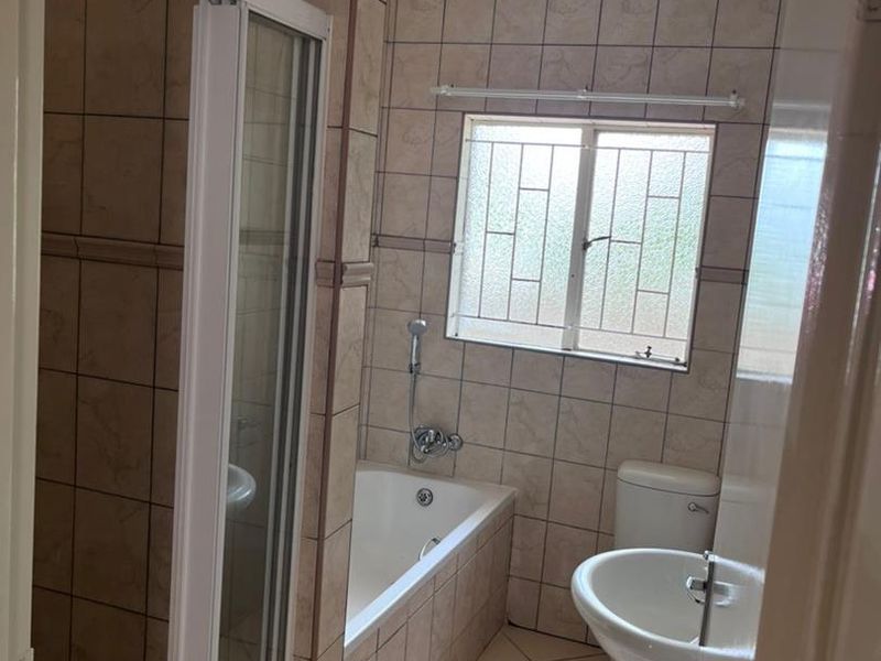 A functional bathroom featuring a shower enclosure, bathtub, pedestal basin, and toilet with neutral wall and floor tiling.
