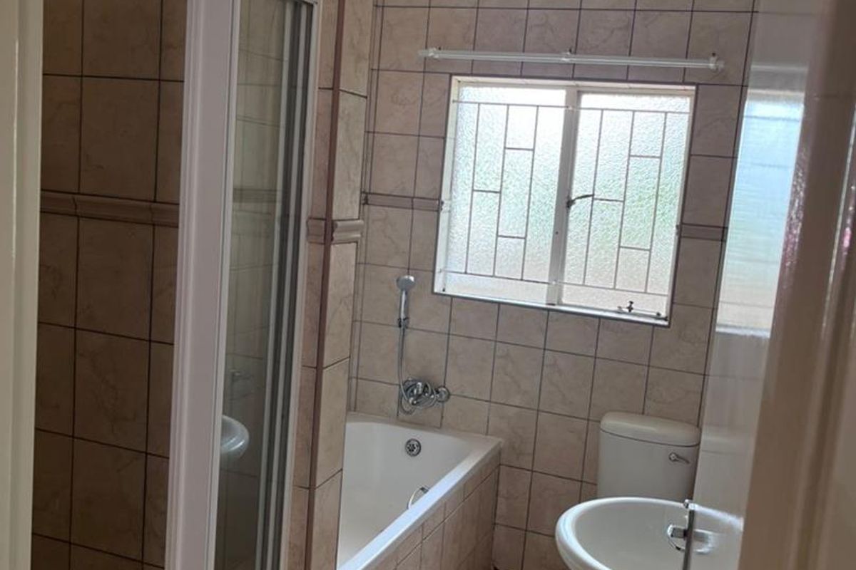 A functional bathroom featuring a shower enclosure, bathtub, pedestal basin, and toilet with neutral wall and floor tiling.