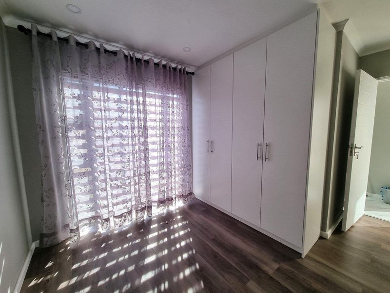 A bright, modern bedroom featuring neutral laminate flooring, ample built-in cupboard storage, and recessed ceiling lighting.