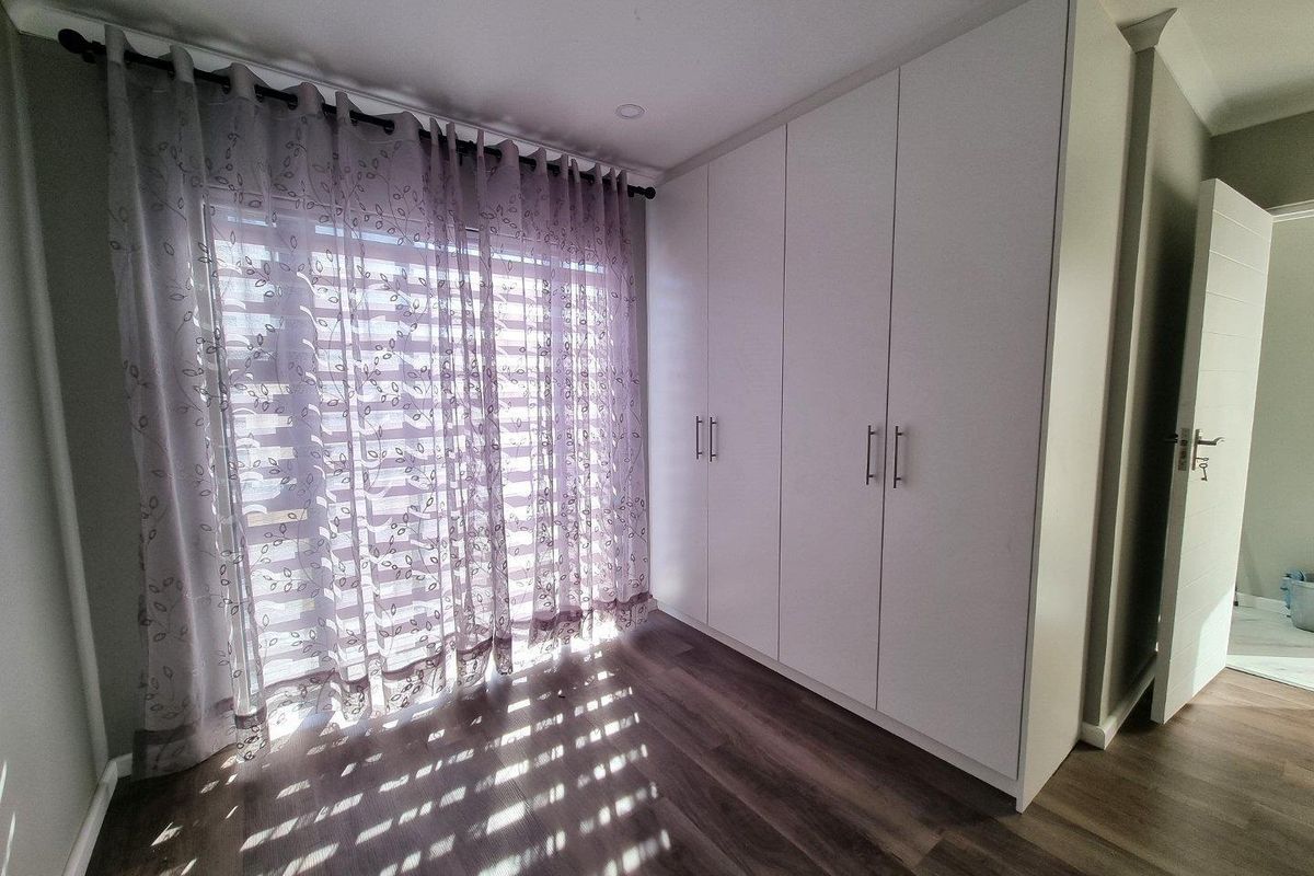A bright, modern bedroom featuring neutral laminate flooring, ample built-in cupboard storage, and recessed ceiling lighting.