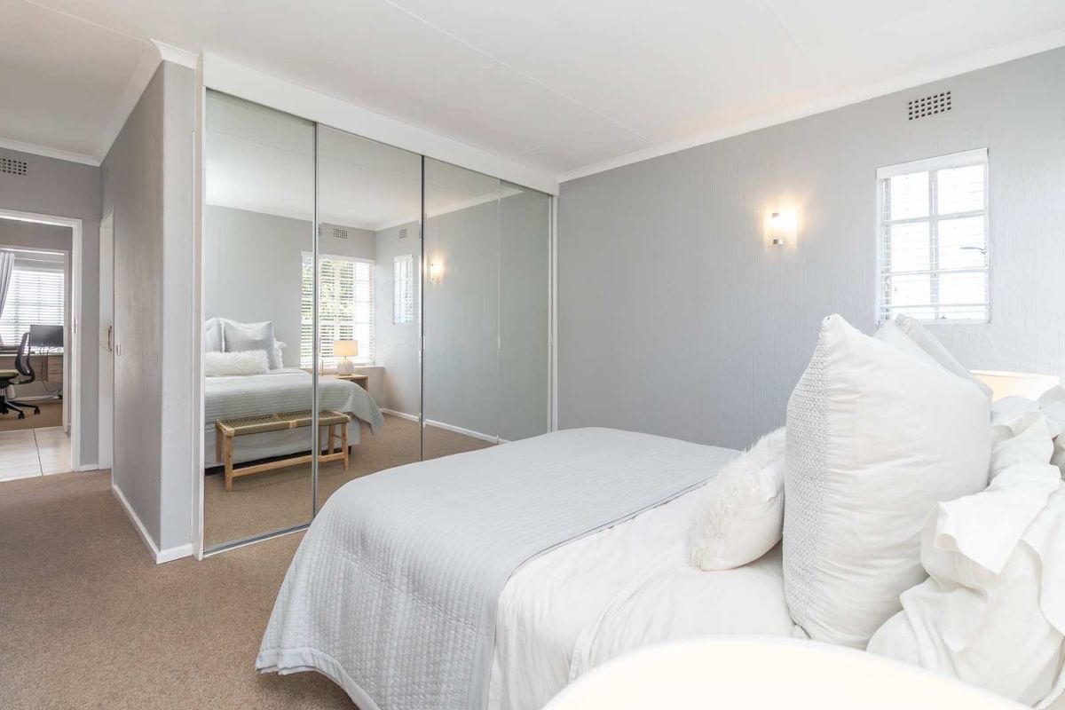 A well-maintained bedroom featuring neutral wall finishes, carpeted flooring, and large floor-to-ceiling mirrored built-in cupboards.