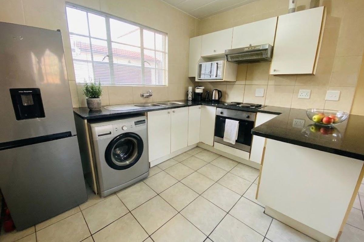 A functional kitchen featuring white cabinetry, dark granite countertops, tiled flooring, and integrated appliances including an oven and extractor fan.