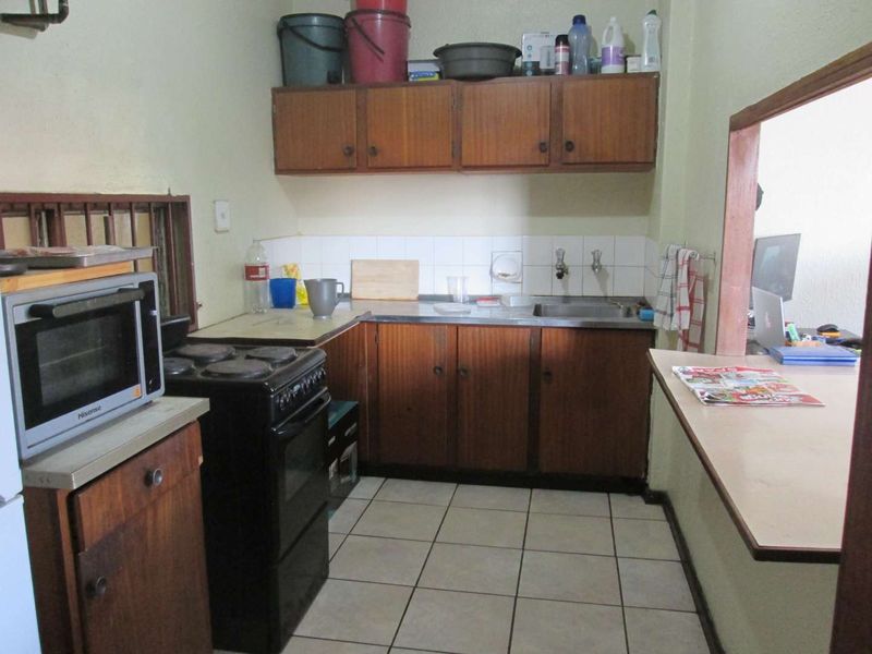 A compact kitchen featuring dated wooden cabinetry, a stainless steel sink, tiled backsplash, and a breakfast counter, offering potential for modernization.