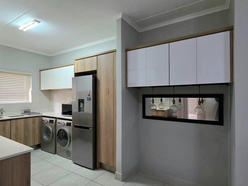Modern kitchen featuring wood-finish cabinetry, white countertops, tiled flooring, and integrated laundry appliances, offering a clean and functional workspace.