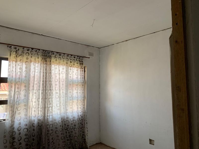 An empty bedroom space featuring plain walls and a window, currently requiring cosmetic repairs and finishing to the ceiling and wall joints.