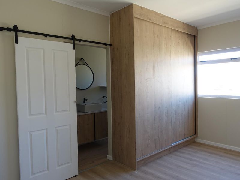 A clean, modern bedroom featuring a large built-in wardrobe, light laminate flooring, and a sliding barn door leading to an en-suite bathroom.