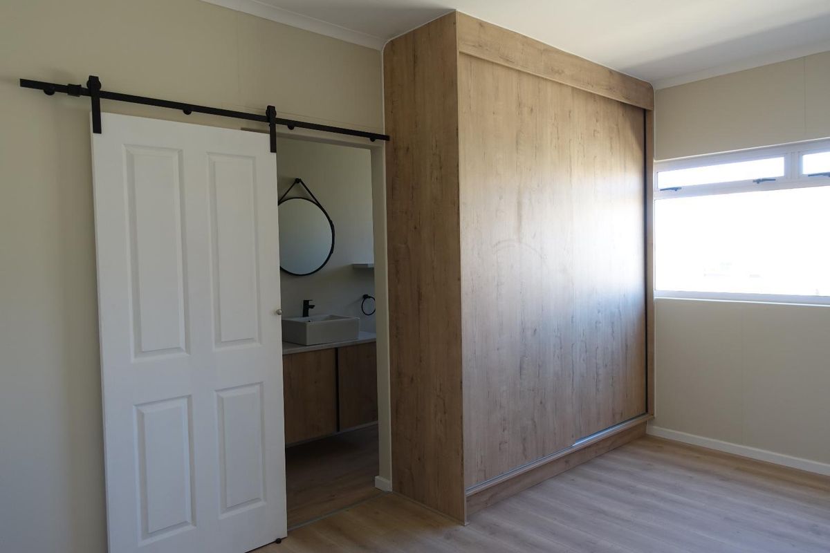 A clean, modern bedroom featuring a large built-in wardrobe, light laminate flooring, and a sliding barn door leading to an en-suite bathroom.