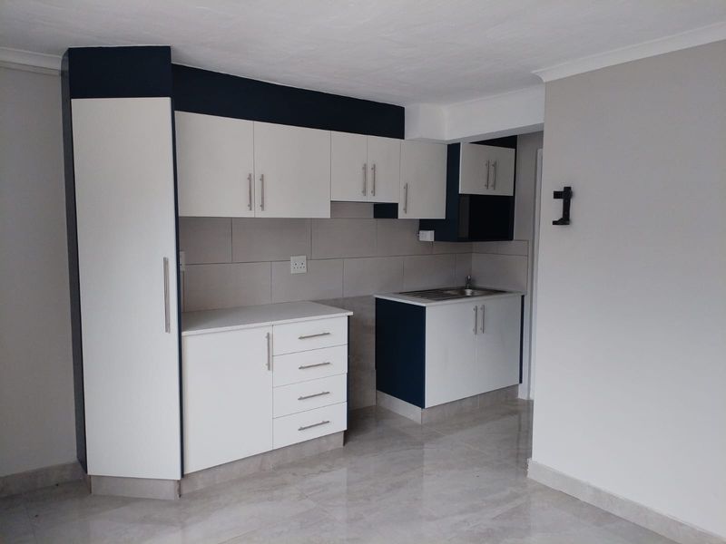 A clean, modern kitchen featuring white and dark blue cabinetry, a tiled backsplash, and neutral floor tiles in an open-plan layout.