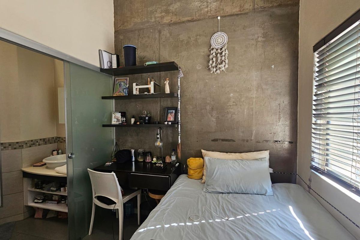 A modern bedroom featuring an exposed concrete feature wall, integrated shelving, and an adjoining bathroom with a glass sliding door.