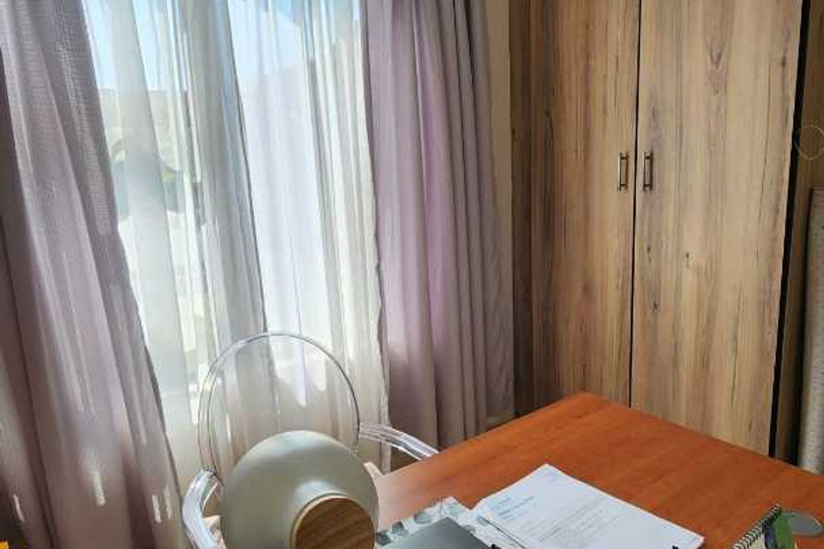A functional bedroom featuring built-in wooden cabinetry and large windows with curtains, providing ample natural light and storage space.