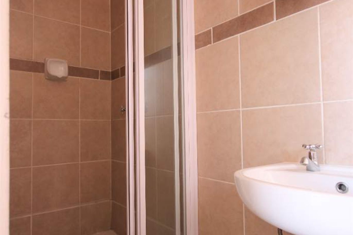 A functional bathroom featuring a shower enclosure with glass door, a pedestal basin, and neutral ceramic wall and floor tiling.