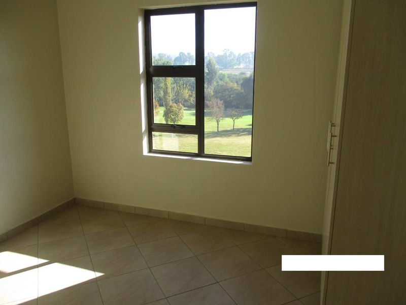 A bright, empty bedroom featuring tiled flooring, a built-in cupboard, and a window offering a pleasant green landscape view.