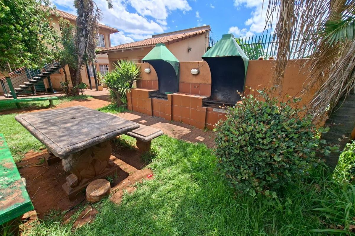 Outdoor communal entertainment area featuring dual built-in brick braai stations with metal hoods, set within a landscaped garden space.