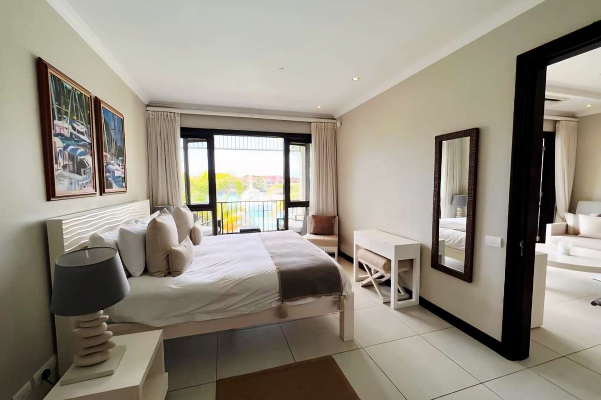 A bright and spacious bedroom featuring tiled flooring, large sliding glass doors leading to a balcony, and an adjoining living area.