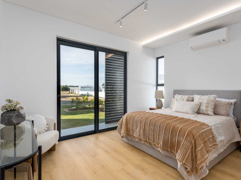 Modern bedroom featuring light wood-look flooring, a split-system air conditioner, and large sliding glass doors providing direct access to the garden.