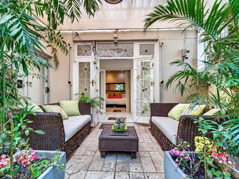 A charming, covered patio area featuring stone paving and elegant french doors leading into the interior living space, surrounded by lush greenery.