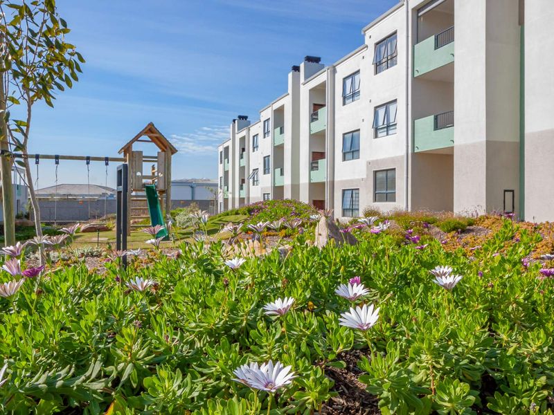 A view of the apartment complex exterior featuring landscaped gardens, a children's play area, and private balconies.