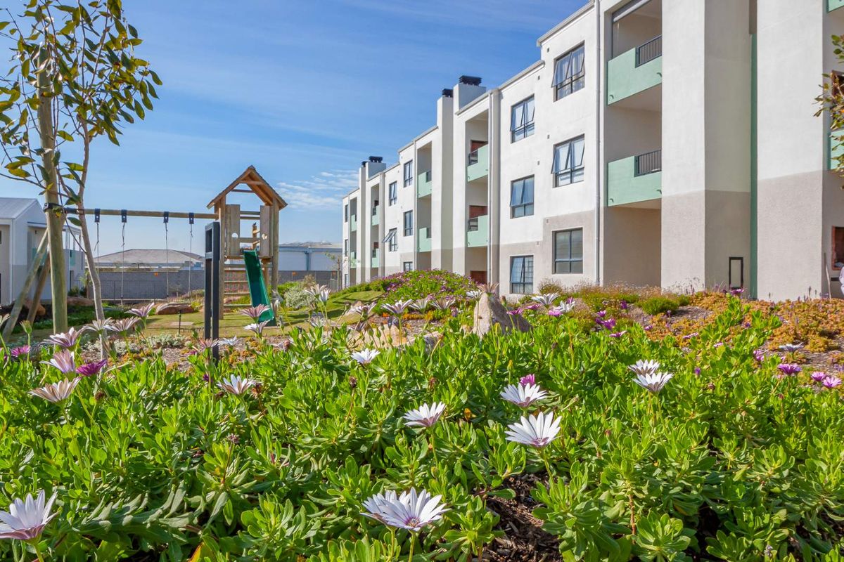 A view of the apartment complex exterior featuring landscaped gardens, a children's play area, and private balconies.