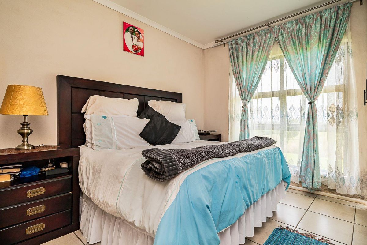 A well-lit bedroom featuring tiled flooring, a large window with curtain tracks, and neutral wall finishes.