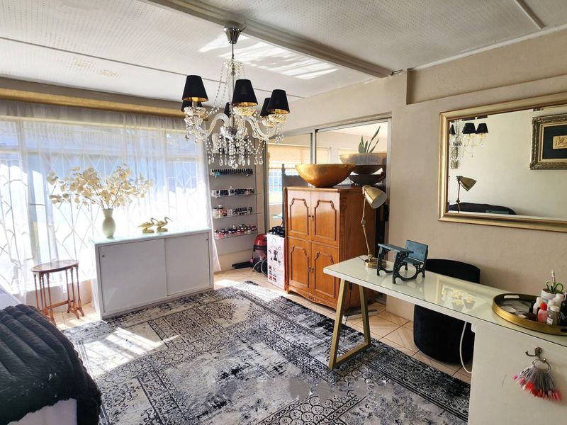 A multi-purpose room featuring tiled flooring, a crystal chandelier, and sliding glass doors, currently utilized as a workspace.