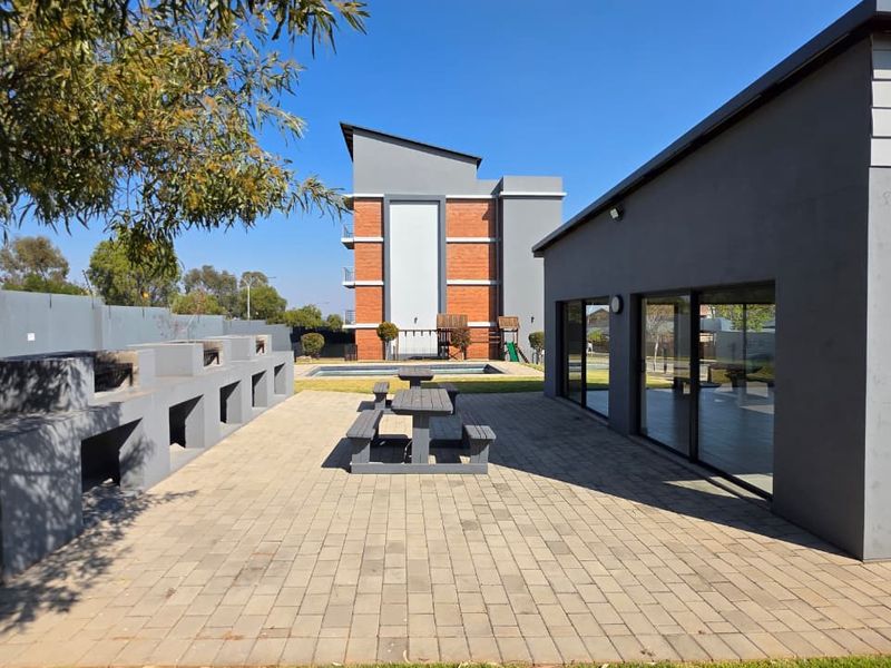 Outdoor entertainment area featuring a paved patio with multiple built-in braai stations, adjacent to a swimming pool and modern apartment building.