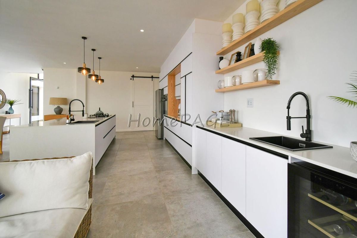 Modern open-plan kitchen featuring sleek white cabinetry, stone countertops, dual sinks, integrated appliances, and stylish pendant lighting with large format floor tiles.