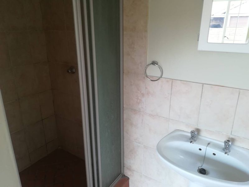 A functional bathroom featuring a shower enclosure and a pedestal basin with tiled wall finishes.