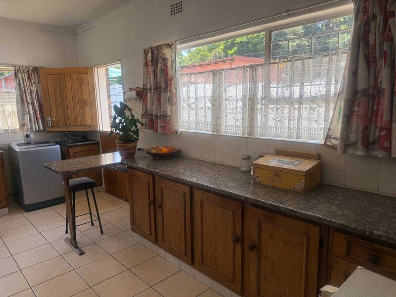 A functional kitchen featuring wooden cabinetry, laminate countertops, and tiled flooring, with a large window providing natural light.