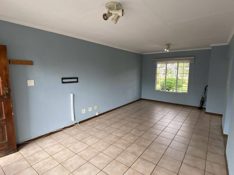 An empty living room featuring tiled flooring, blue painted walls, and a window with a roller blind.