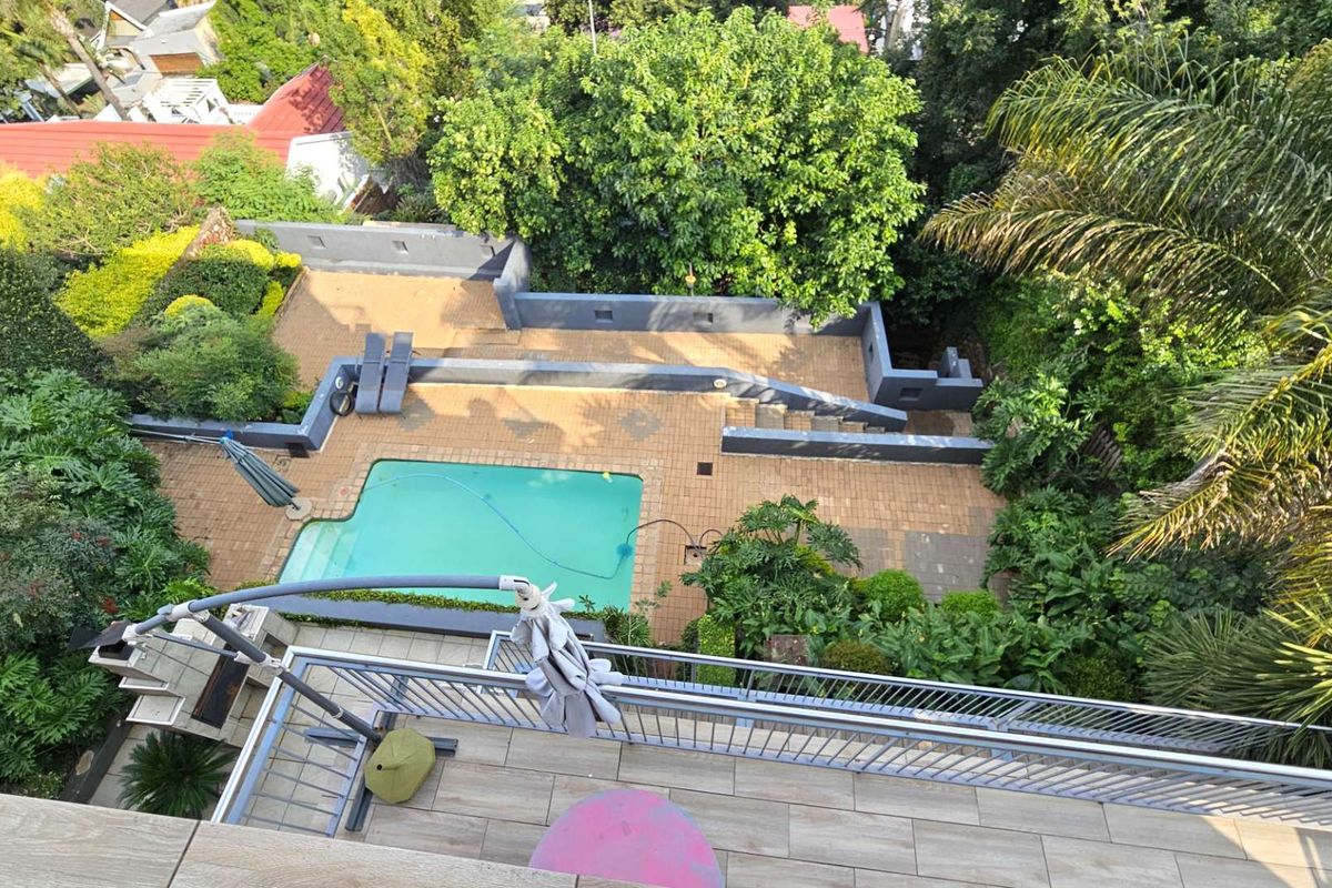 Elevated view of a private backyard featuring a swimming pool, paved patio area, retaining walls, and lush surrounding garden landscaping.