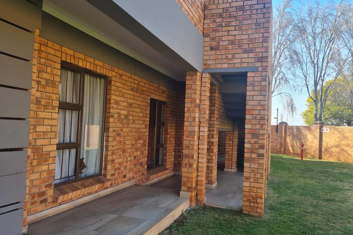 A view of the exterior facade featuring face brick construction, tiled patio area, and access to a shared garden space.