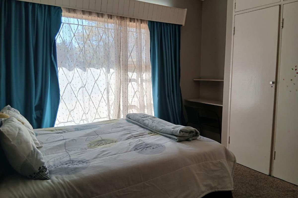 A bedroom featuring a built-in wardrobe, integrated desk space, and security gate on the window, offering a functional layout with dated finishes.