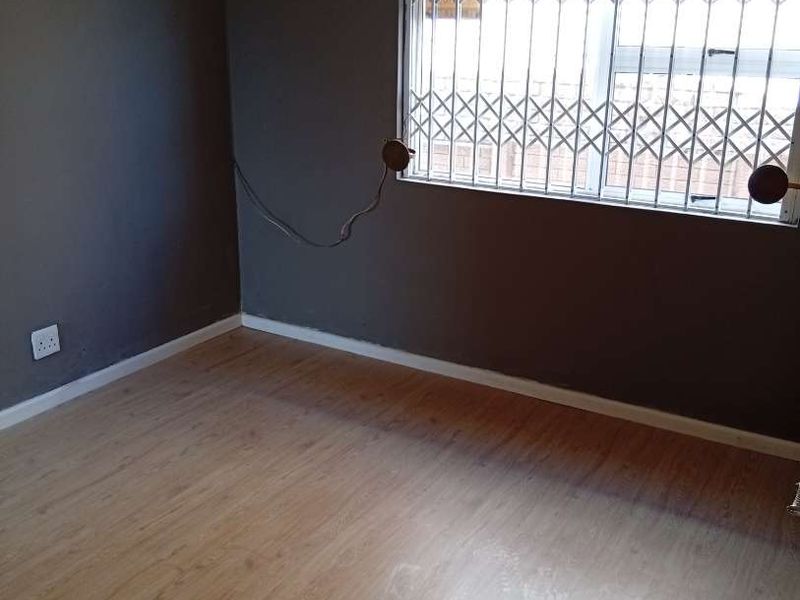An empty bedroom featuring laminate flooring, dark painted walls, and a window fitted with security bars and a metal gate.