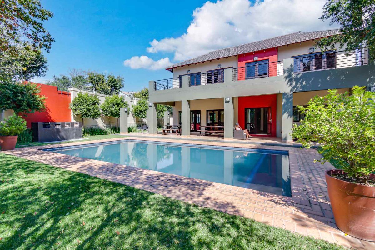 A spacious rear exterior view featuring a large swimming pool, manicured lawn, and a two-story building with a covered patio and balcony.