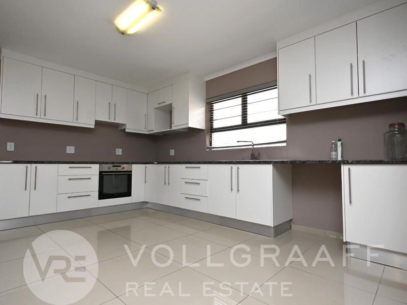 A clean, modern kitchen featuring white cabinetry, granite countertops, built-in oven, and tiled flooring, offering a functional and well-maintained workspace.