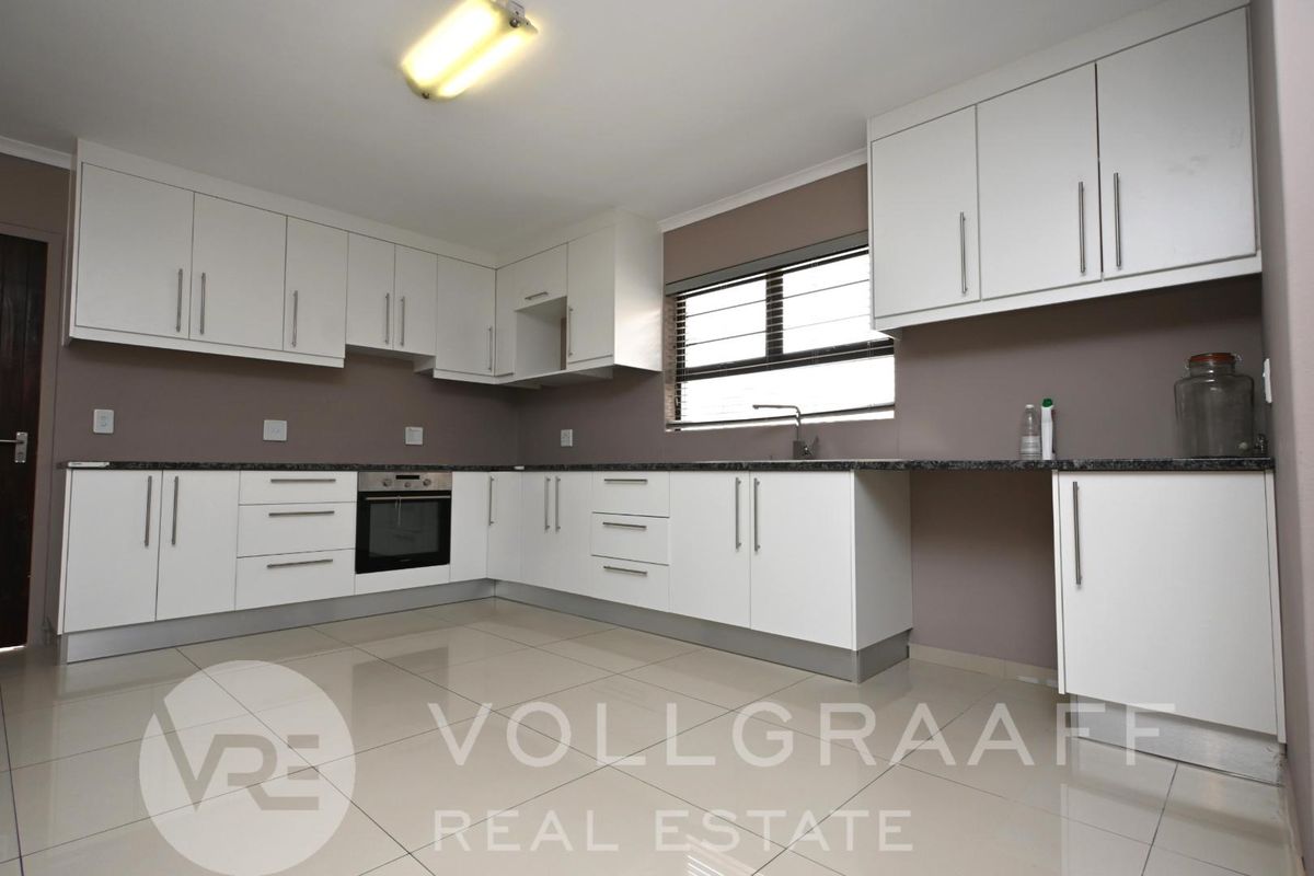 A clean, modern kitchen featuring white cabinetry, granite countertops, built-in oven, and tiled flooring, offering a functional and well-maintained workspace.