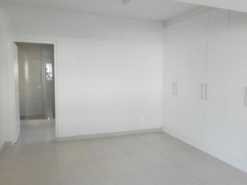 A bright, empty bedroom featuring neutral tiled flooring, ample built-in cupboard storage, and direct access to an en-suite bathroom.