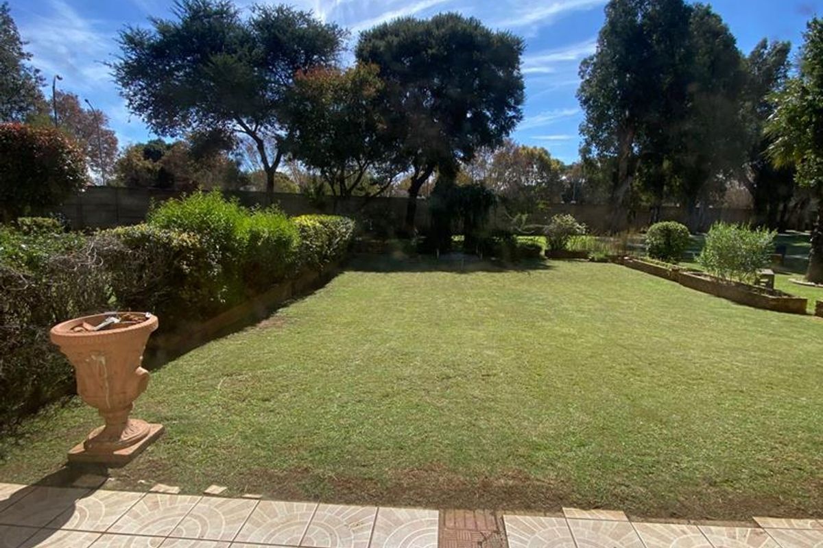A private rear garden featuring a tiled patio area overlooking a well-maintained lawn and established perimeter hedging.